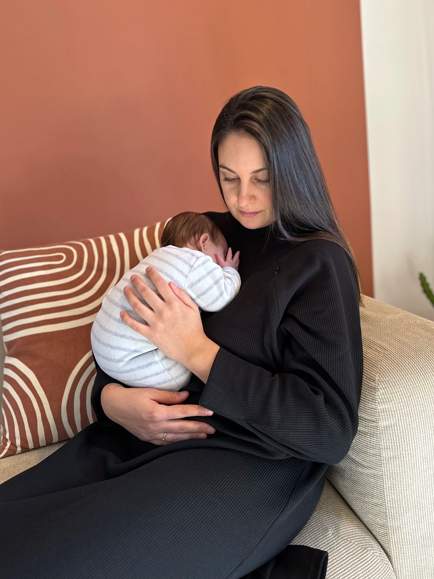Modèle portant un bébé dans les bras dans la robe longue noire pour allaiter en maille ouverture à zip nuance lactée